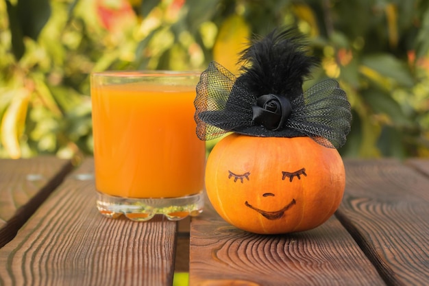 Pumpkin with a cute face in a woman's hat on the background of a glass of juice Selective focus