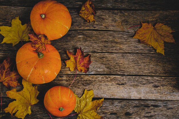 Pumpkins and fallen autumn foliage wooden background