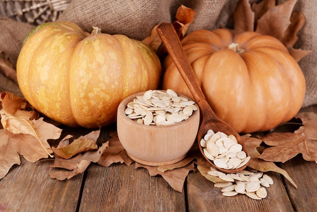 Pumpkins and pumpkin seeds in bowl on wooden background