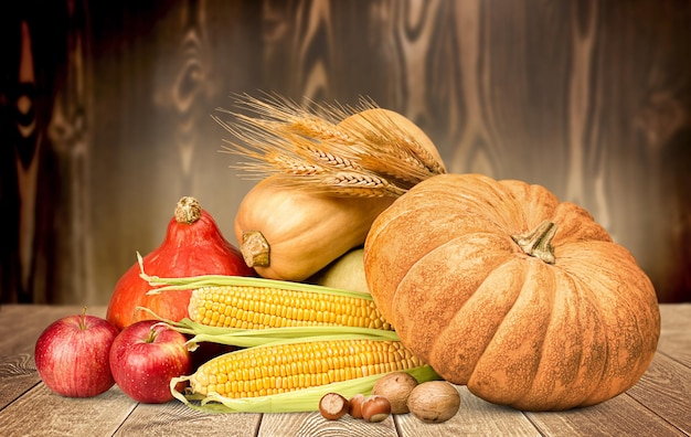 Pumpkins spikelets of wheat corn cobs apples and nuts on a wooden background