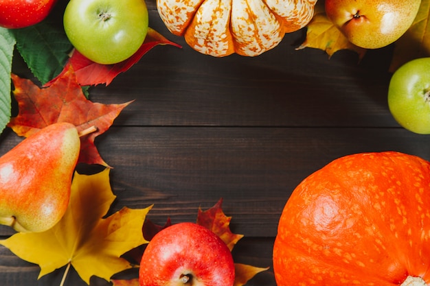 Pumpkins with colorful maple leaves, ripe apples and pear on dark wooden background