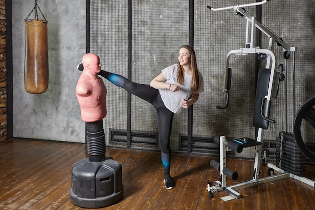 Punching bag bob dummy in gym young woman kicks