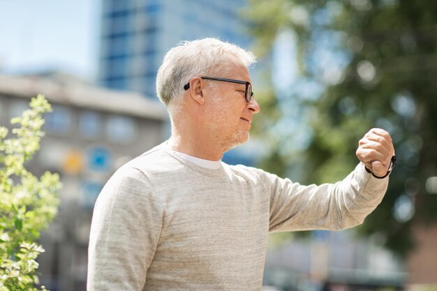 写真 時間厳守と人々のコンセプト – 年配の男性が街で腕時計やスマートウォッチを手にして時間をチェックする