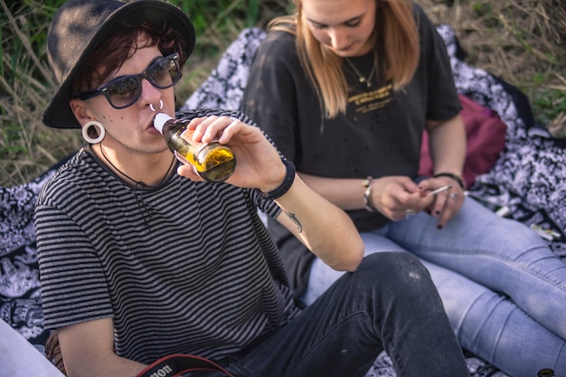 Punk boy drinks beer sitted in a outdoor park