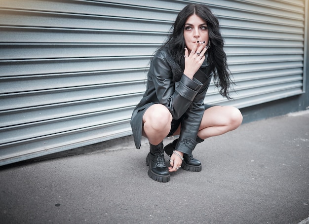 Punk emo and woman smoking a cigarette in the street of an urban city in Canada in an edgy black outfit Grunge rocker and girl smoker with tobacco to smoke while sitting in the road in town