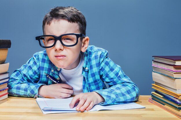 Pupil in glasses squints, bad vision concept. Young schoolboy sitting at the desk against many books