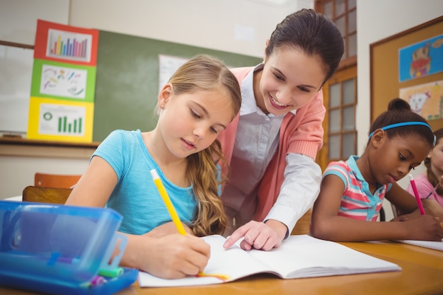 Pupil and teacher at desk in classroom at the elementary school