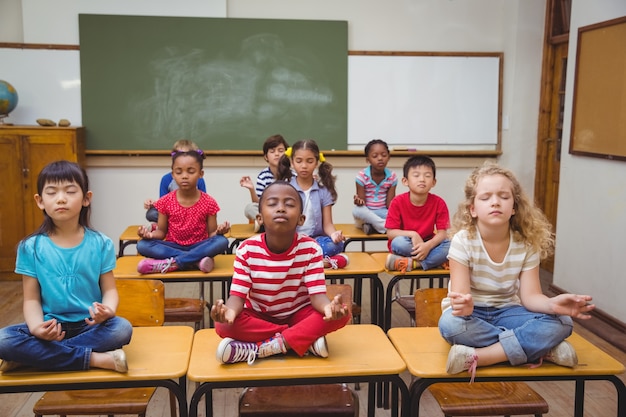 Photo pupils meditating in lotus position on desk in classroom