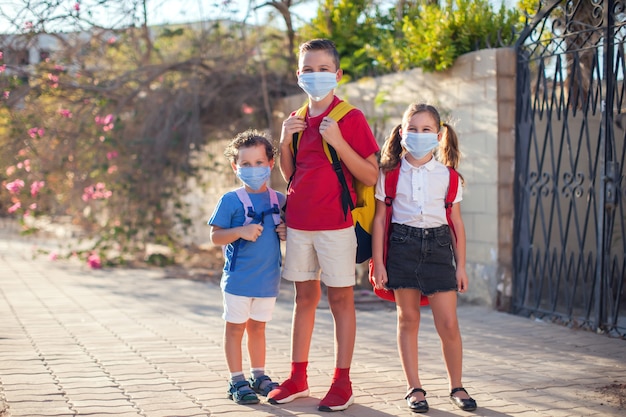 顔と屋外のバックパックに医療用マスクを持つ生徒。コロナウイルス期間中の教育。子供とヘルスケア。学校に戻る。