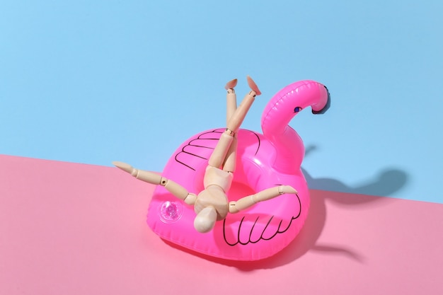 Photo puppet mannequin with inflatable flamingo on pink blue bright. beach vacation concept. summer rest. minimalism