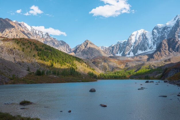 写真 純な青いアルプス湖 森の丘と巨大な雪の山を眺める 秋の晴れた日に 氷河湖 巨大な雪に覆われた山脈に照らされた明るい太陽 鮮やかな秋の色 高い山々