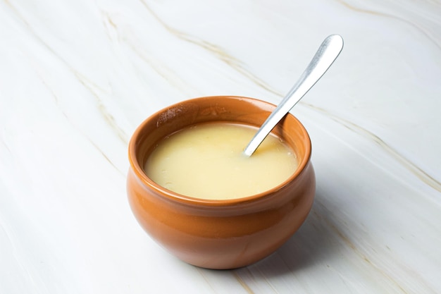 Pure cow ghee in ceramic bowl with steel spoon on white background