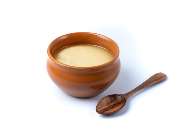 Pure cow ghee in ceramic bowl with wooden spoon on white background