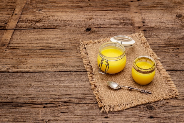 Pure or desi ghee (ghi), clarified melted butter. Healthy fats bulletproof diet concept or paleo style plan. Glass jar, silver spoon on vintage sackcloth.