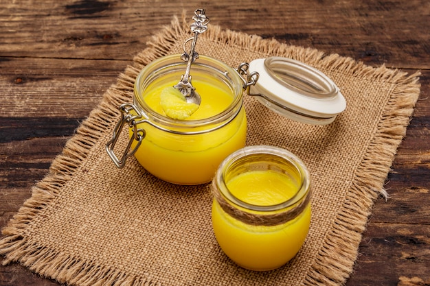 Pure or desi ghee (ghi), clarified melted butter. Healthy fats bulletproof diet concept or paleo style plan. Glass jar, silver spoon on vintage sackcloth.
