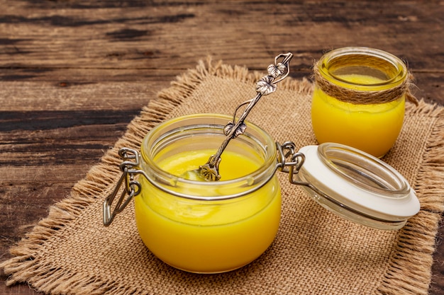 Pure or desi ghee (ghi), clarified melted butter. Healthy fats bulletproof diet concept or paleo style plan. Glass jar, silver spoon on vintage sackcloth.