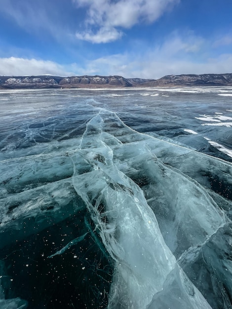 Pure ice of the frozen lake Baikal against the background of mountains frozen winter Baikal