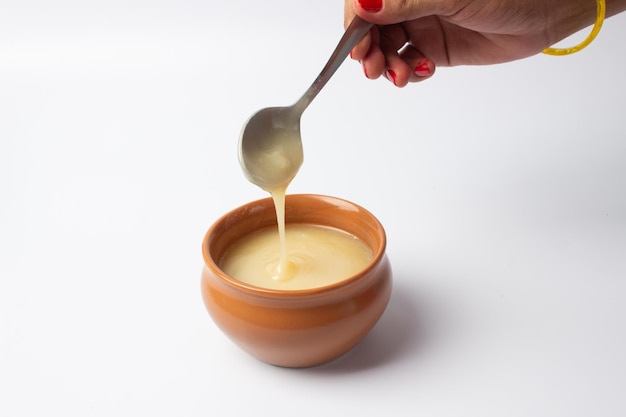 Pure koe ghee in keramische kom op witte achtergrond met ghee-lepel in de hand