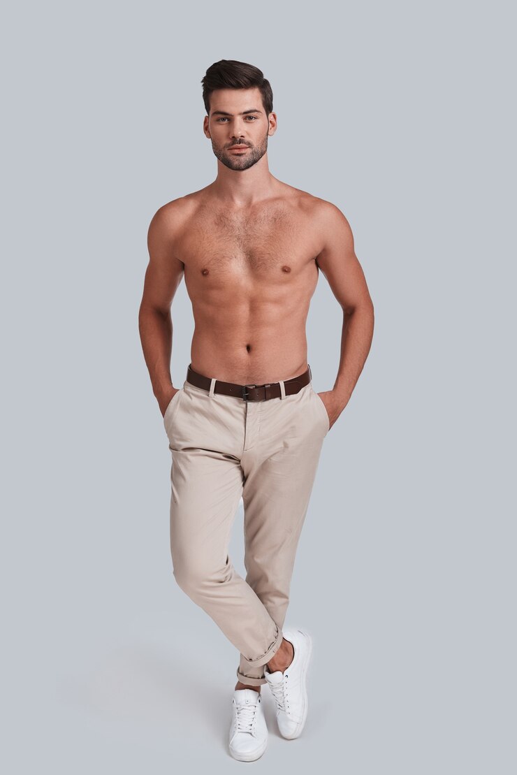 Photo pure perfection. full length of shirtless handsome young man keeping hands in pockets head and looking at camera while standing against grey background