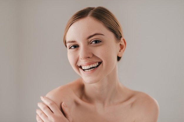 Pure schoonheid. Portret van een aantrekkelijke jonge vrouw met sproeten op het gezicht die lacht en naar de camera kijkt terwijl ze tegen een grijze achtergrond staat