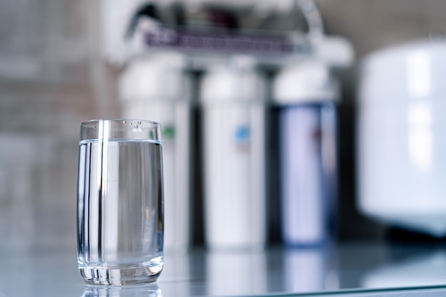 Pure water in glass and water filters on the blurred background. Household filtration system.