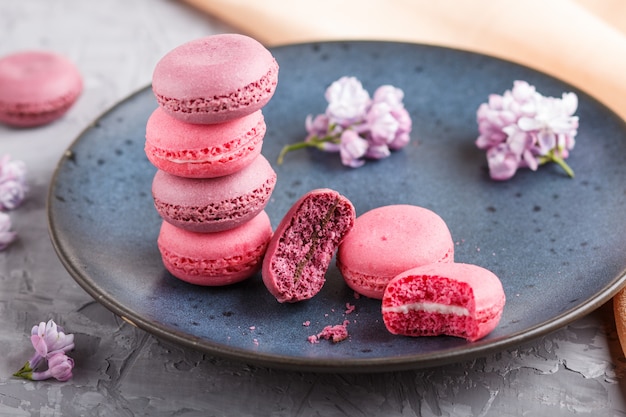 Purpere en roze macaron of makaroncakes op blauwe ceramische plaat op grijs beton.