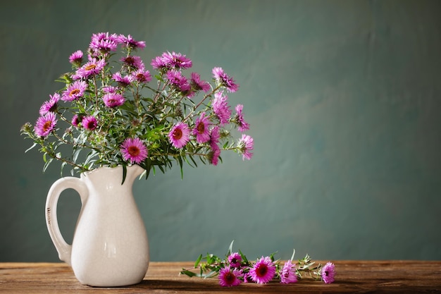 Purple autumn flowers in jug on dark old background