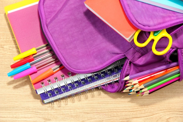 Purple backpack with school supplies on wooden background