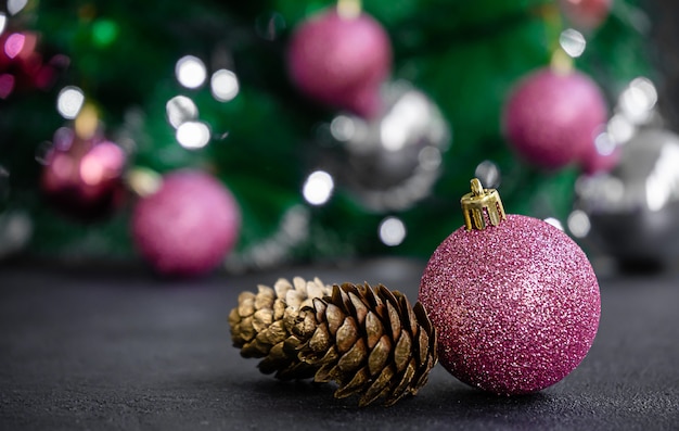 Purple bauble and golden colored pine cone on blurred Christmas lights background