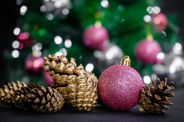 Purple bauble and golden colored pine cones on blurred Christmas tree background