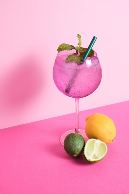 purple cocktail glass with mint and fruits on pink background