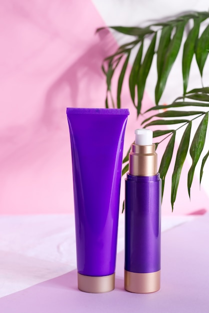 Purple cosmetic plastic bottles for cream and lotion with green herbal leaves and flowers on a tricolor