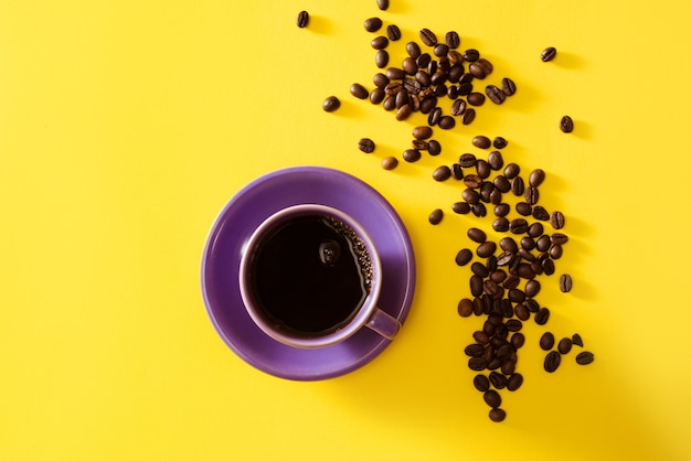 黄色の背景にコーヒー豆とコーヒーの紫色のカップ