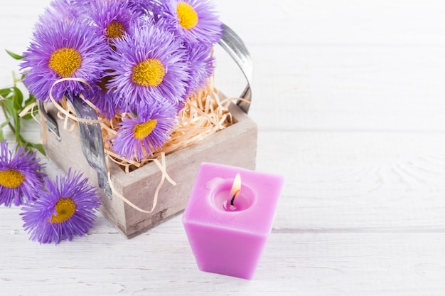 Purple daisies and lit candle on white table