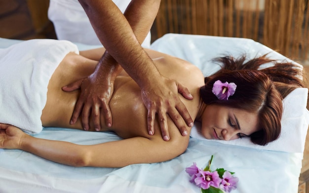 Лежащий фиолетовый цветок Мужчина делает массаж молодой женщине в белом полотенце в помещении
