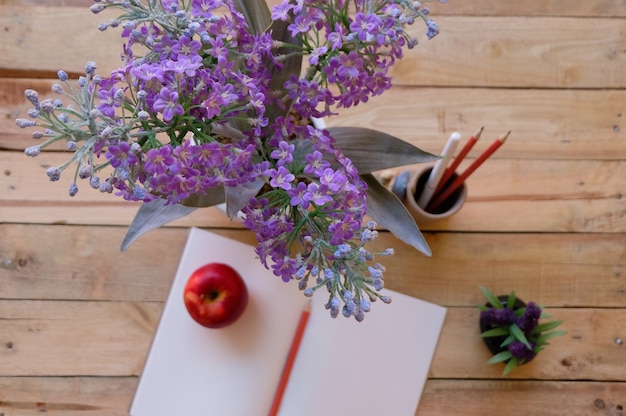 purple flowers, blank note book, apple and pencils on wood background