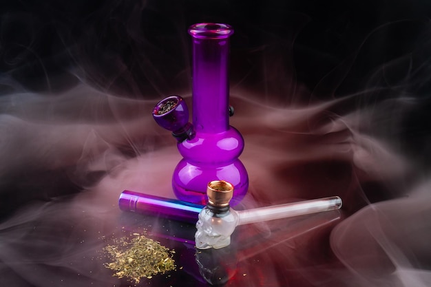 Photo purple glass bong with pipe and pile of weed drug tools for marijuana use