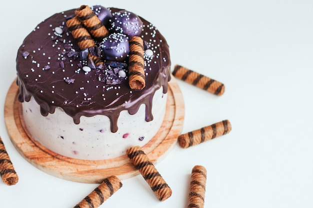 Фиолетовый блеск черничный торт с шоколадной глазурью на белой поверхности копией пространства. домашний шоколадный торт с черникой и полосатыми вафельными трубочками.