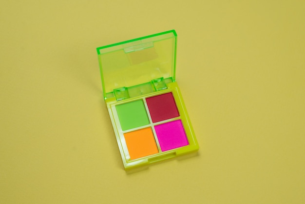 Purple, green, orange and blue eye shadow palette on a green background. Make up. Neon colours.