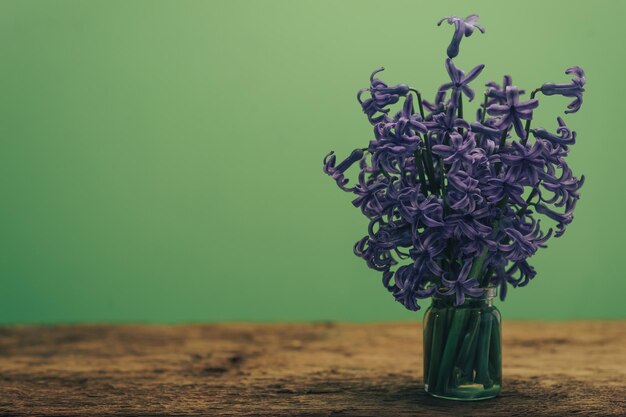 古い木製のテーブルの上にある花瓶の中の紫のヒアシンスの花 緑の壁の背景