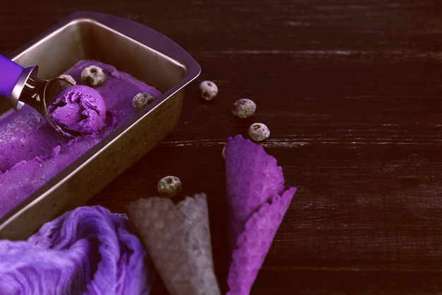 Purple ice cream with a spatula for ice cream on a dark wooden background with waffle cups