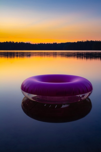 Purple inflatable swimming ring on top of still lake water surface at sunset