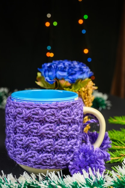 Purple knitted mug with pompoms. Christmas and New Year concept on black background.