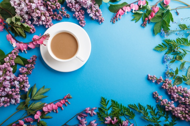 Purple lilac and bleeding heart flowers and a cup of coffee on pastel blue. 