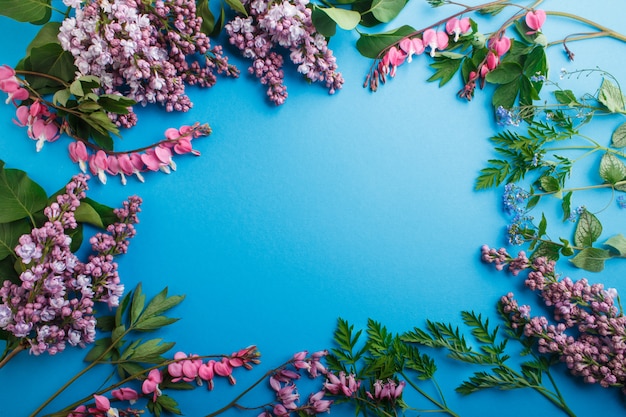 Purple lilac and bleeding heart flowers on pastel blue background. 