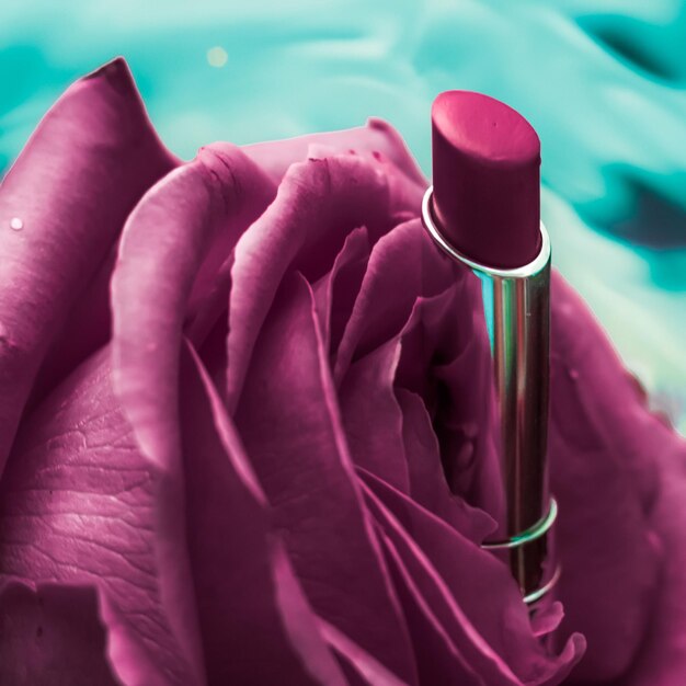 Purple lipstick and rose flower on liquid background waterproof\
glamour makeup and lip gloss cosmetics product for luxury beauty\
brand holiday design