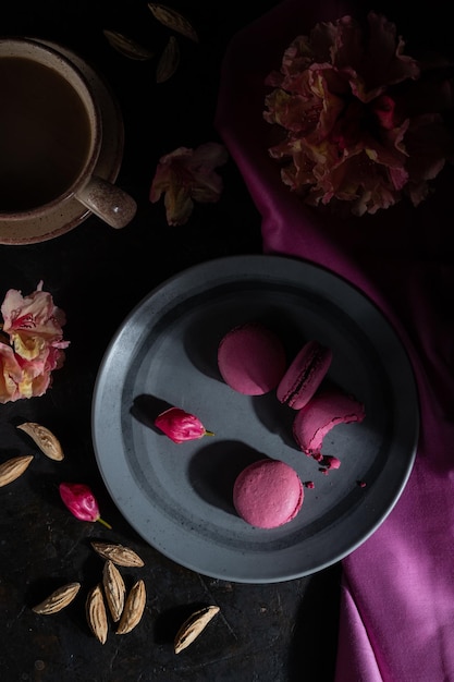 Purple macarons or macaroons cakes with cup of coffee on a black concrete background Hard light low key Top view