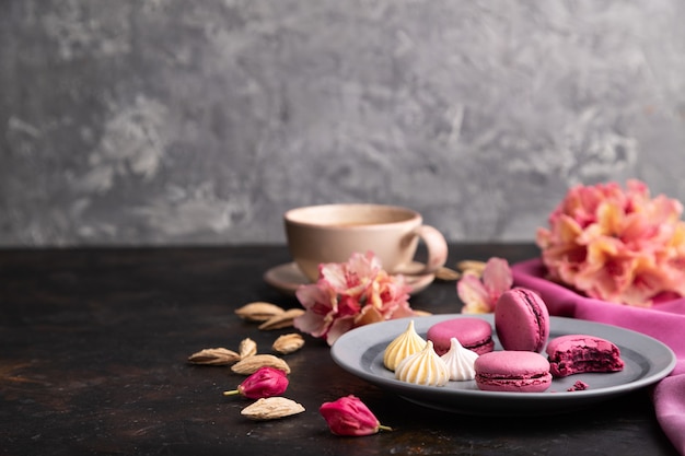 Purple macarons or macaroons cakes with cup of coffee on a black concrete surface and pink textile