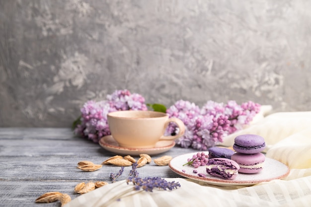 Purple macarons or macaroons cakes with cup of coffee on a gray wooden surface and white linen textile