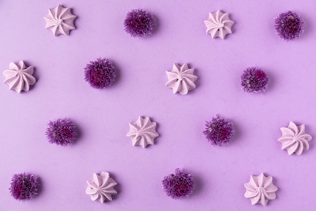 Purple meringue and purple allium flowers on purple background food and floral pattern flat lay top view